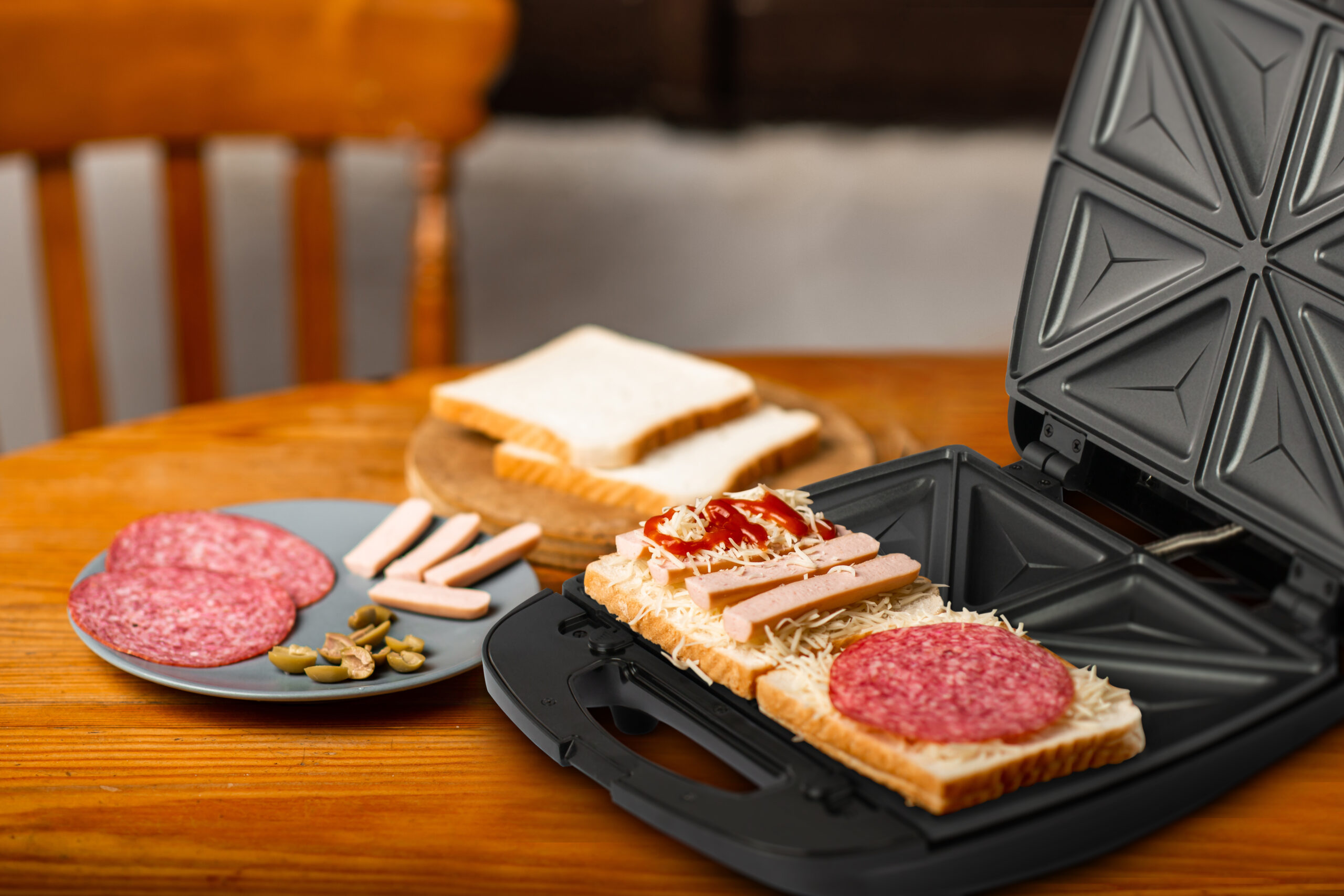 Sandwich maker and sandwich making. Different ingredients lie side by side on wooden table.